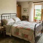 Cozy cottagecore bedroom with an iron bed, linen bedding and dried flowers by the window